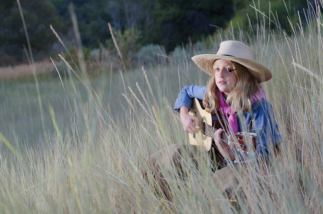 Young cowgirl playing guitar outdoor demonstrating proper outdoor lighting for portrait photography by Sara Collier of Brenham Texas