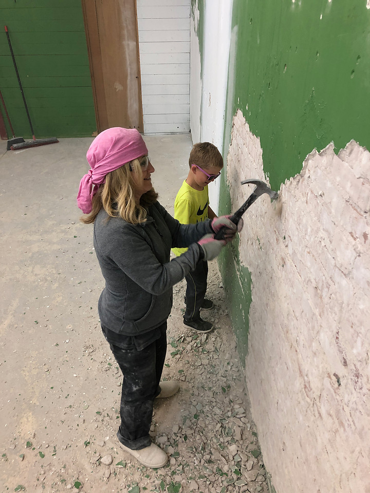 Working Granny and grandson hammer plaster off a wall to expose the brick underneath